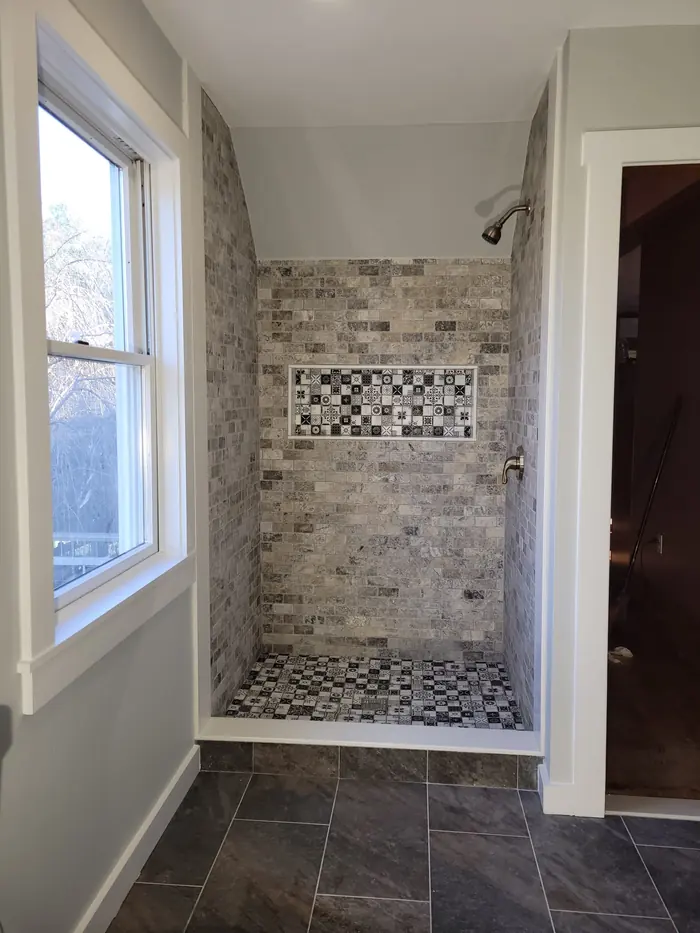 Bathroom under a sloped ceiling with stone tile shower, mosaic niche and dark plank floor tile