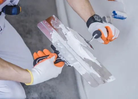 Gloved hands loading joint compound onto a taping knife for plaster and drywall repair