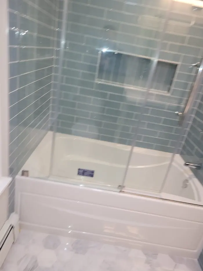 Close view of a soaking tub with blue glass subway tile walls and recessed shelf niche