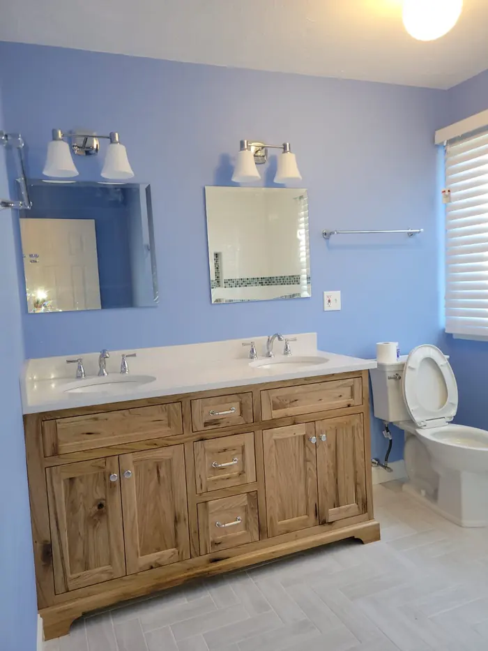 Bathroom remodel with a rustic wood double vanity, white quartz top, two mirrors and periwinkle blue walls