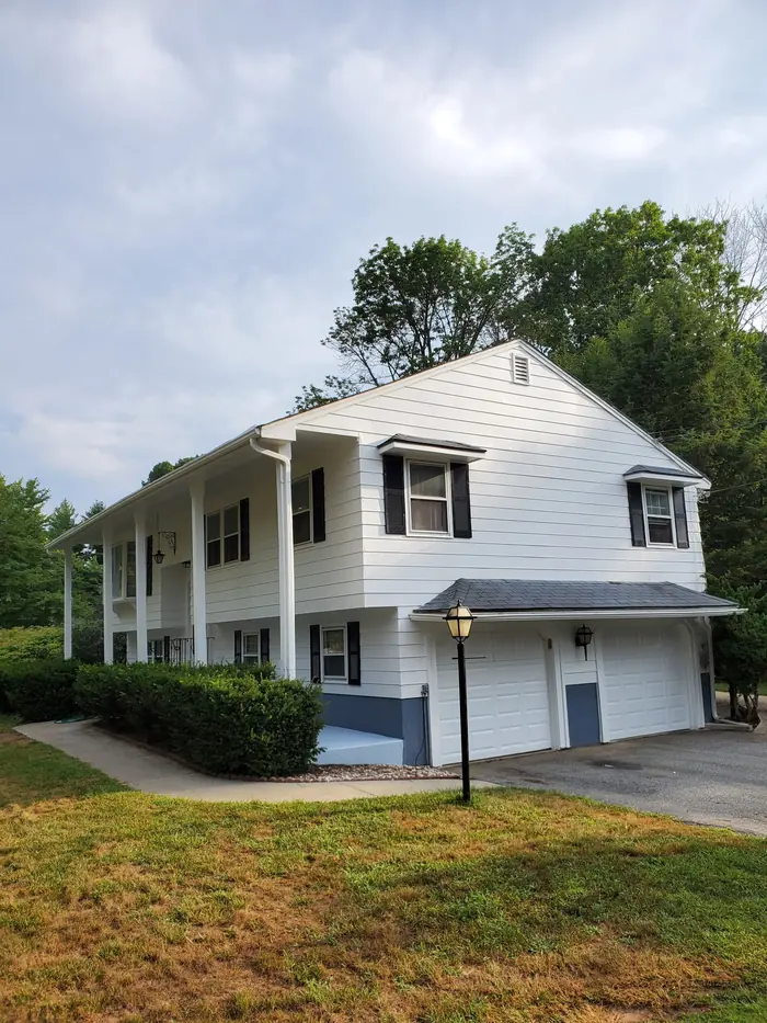 White split-level home after exterior painting, with blue painted foundation and fresh white trim