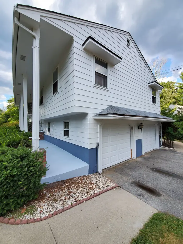 Side of a white house with freshly painted siding and blue foundation band along the driveway