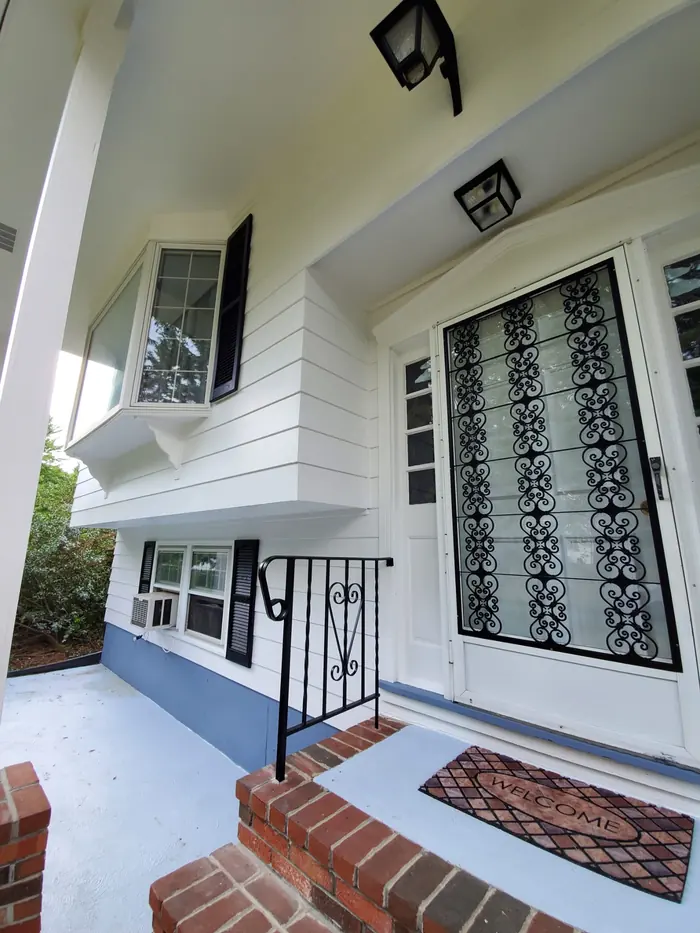 Front porch of a white split-level with brick steps, black railing and freshly painted porch floor