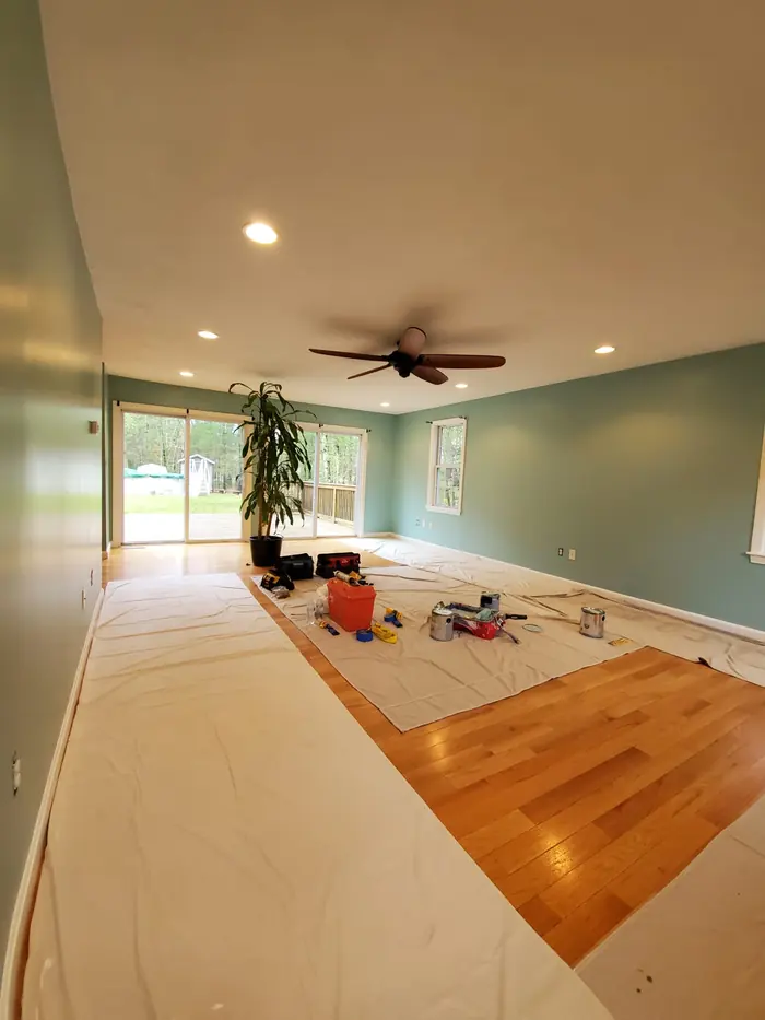 Living room with paper floor protection partly removed, showing new finish on the hardwood and sage green walls