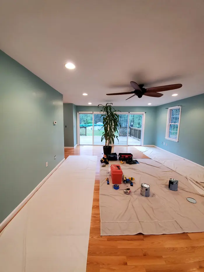 Long living room during painting with drop cloths covering the hardwood floor and freshly painted sage green walls
