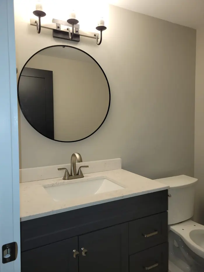 Bathroom with navy blue vanity, white top, round black mirror and three-light vanity fixture
