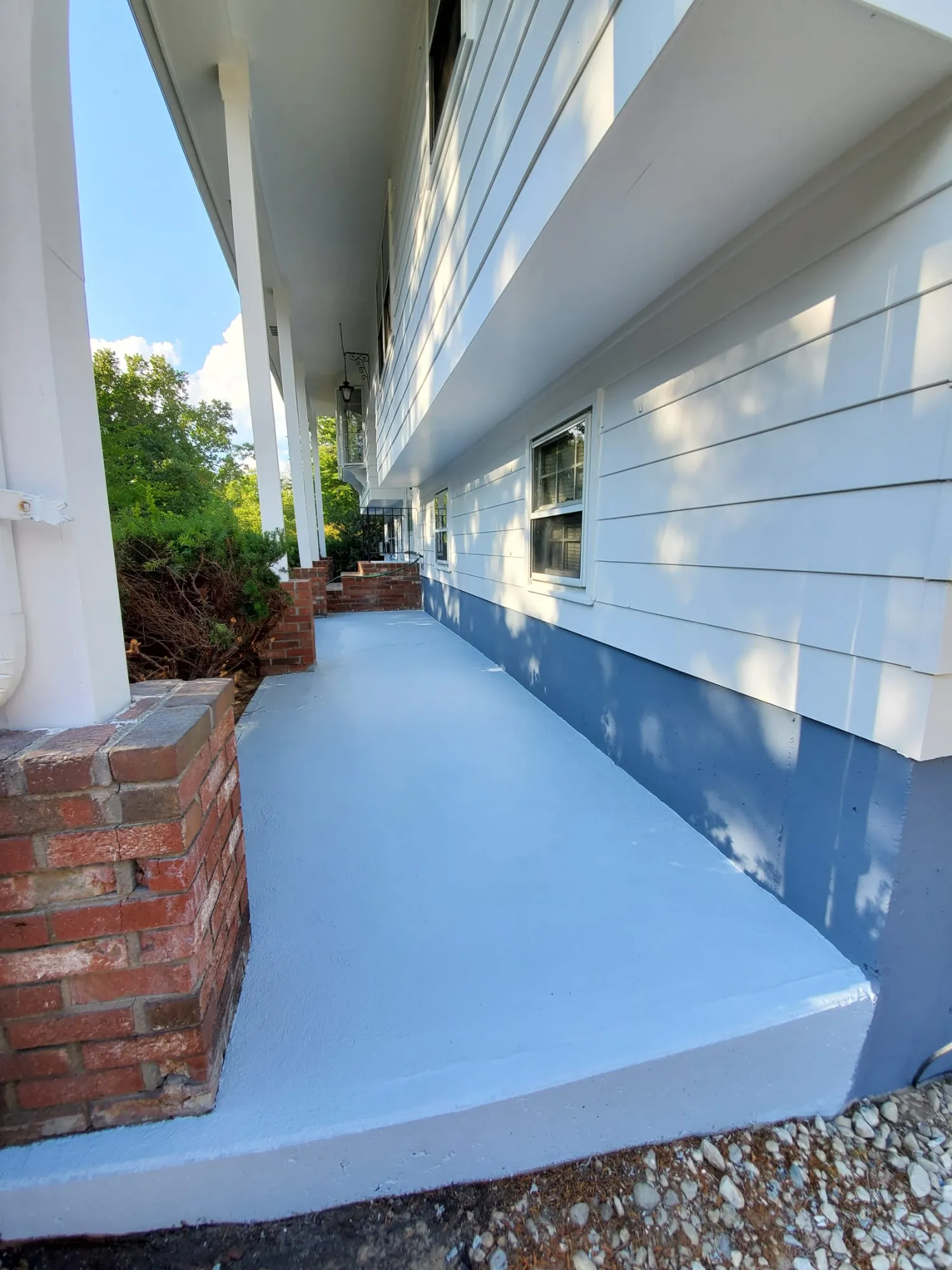 Painted concrete walkway and blue foundation running along the white siding of a house