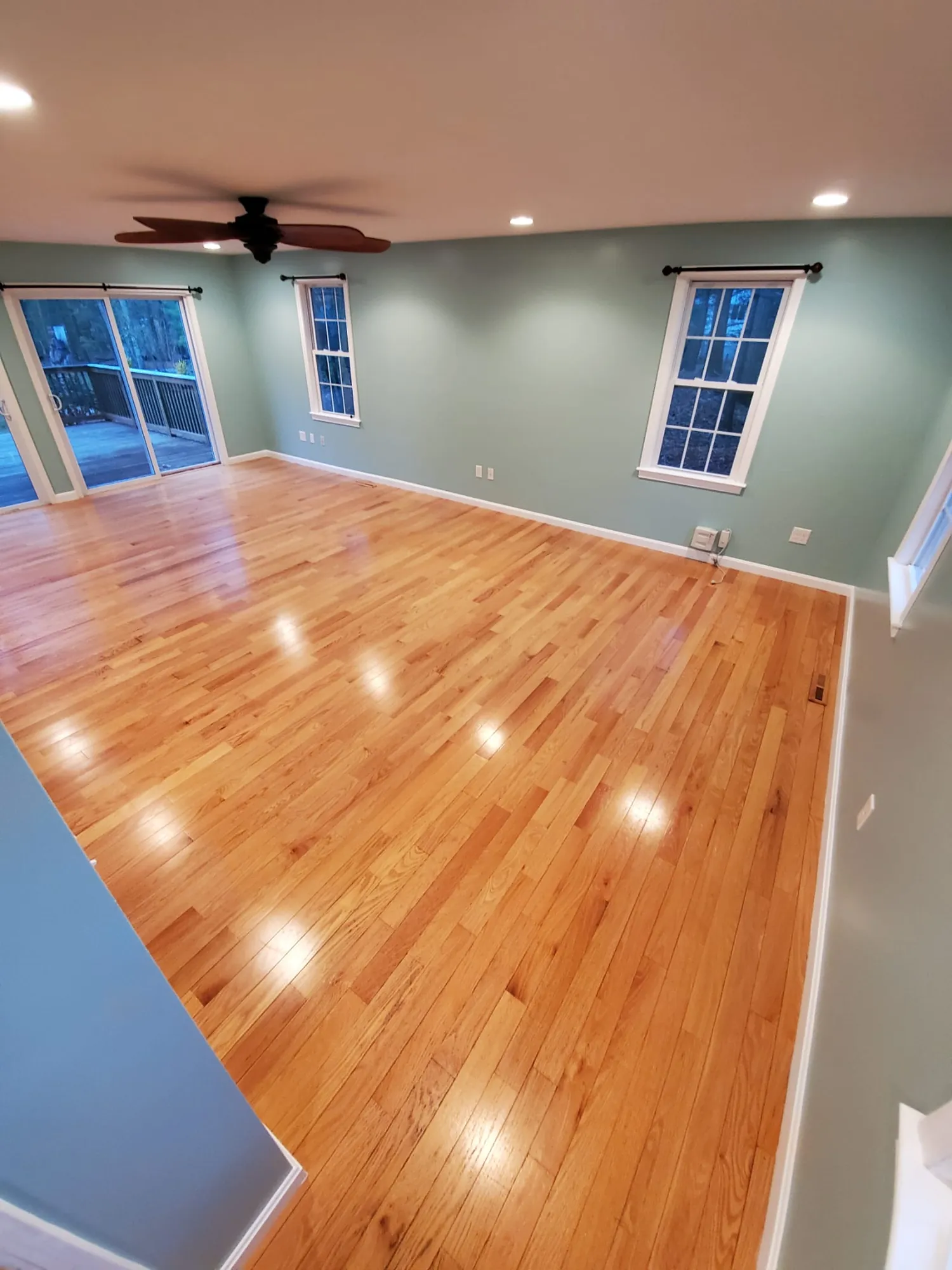 Wide view of a finished great room with refinished hardwood floor, sage green walls, recessed lights and ceiling fan