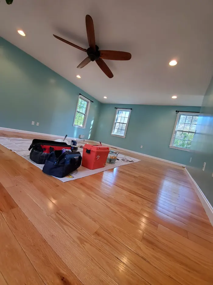 Sage green room with recessed lights, ceiling fan and tool bags on the hardwood floor before cleanup