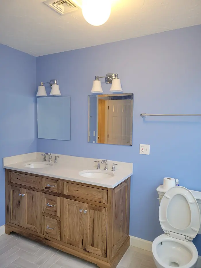 Wide view of a blue bathroom with rustic wood double sink vanity, chrome fixtures and light tile floor