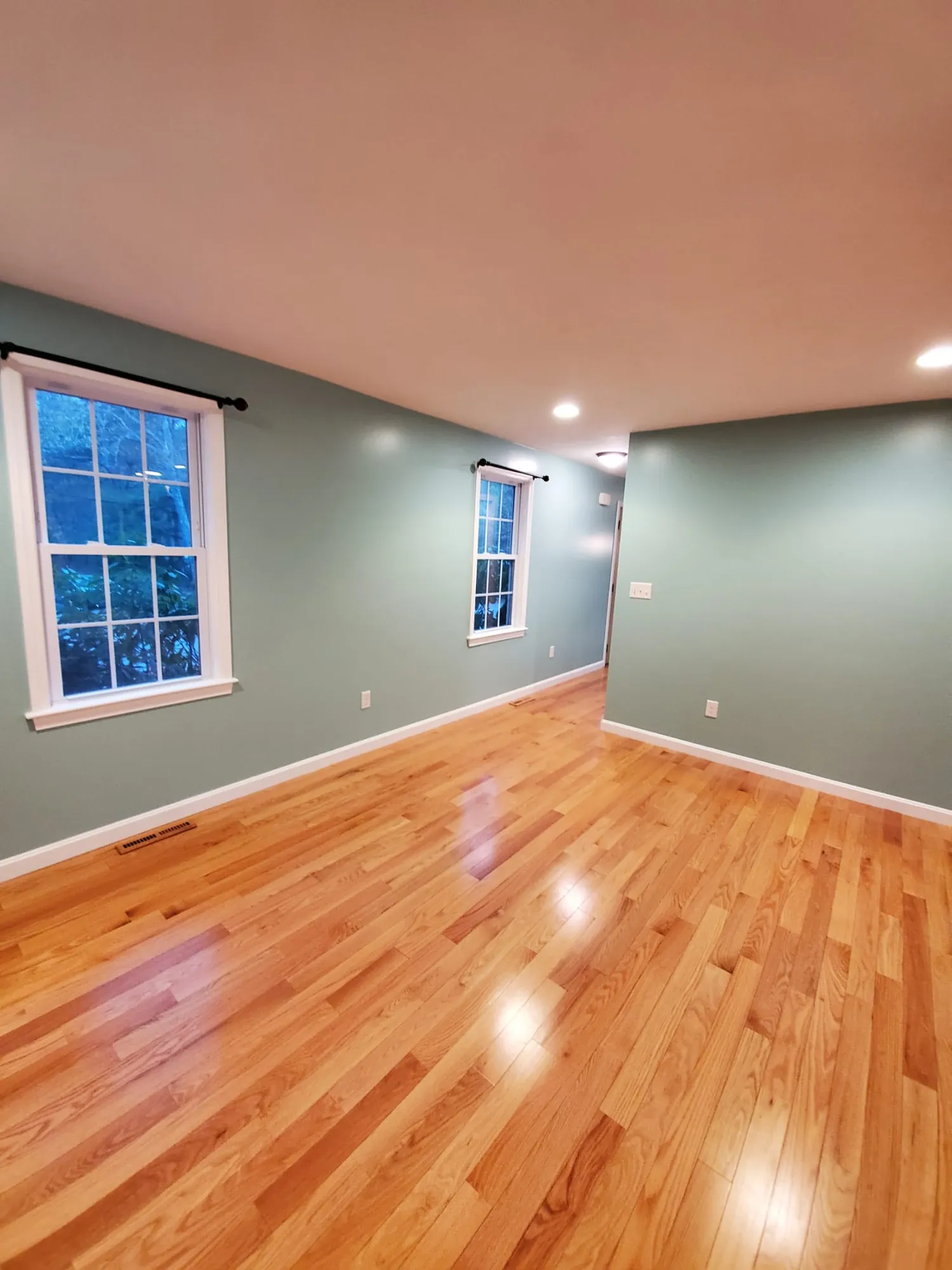 Finished room with sage green walls, white trim, black curtain rods and glossy refinished red oak floor