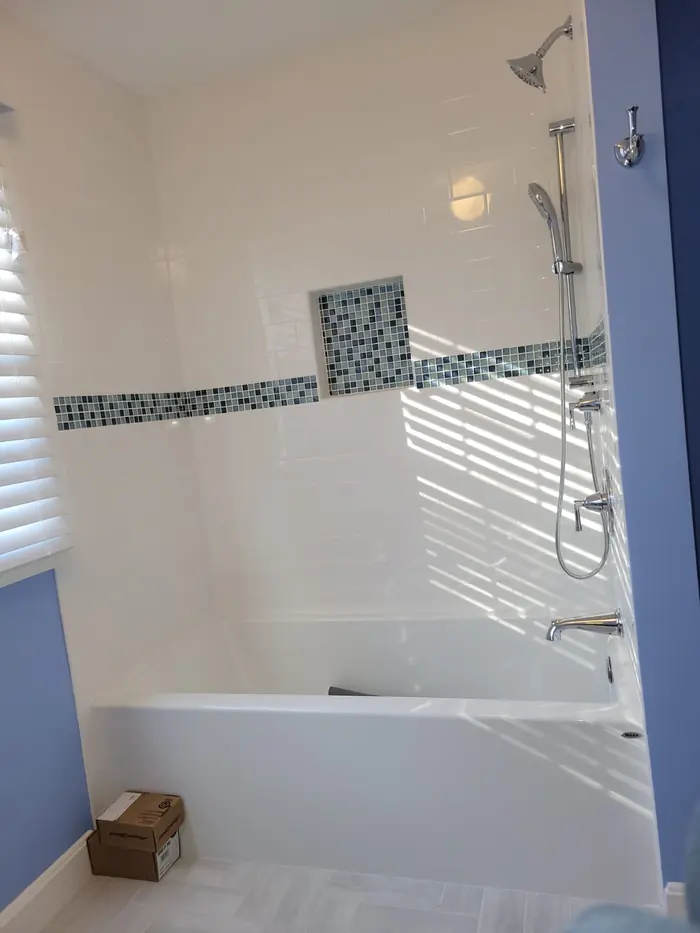 Tub and shower surround in white tile with a blue glass mosaic accent band and matching mosaic niche