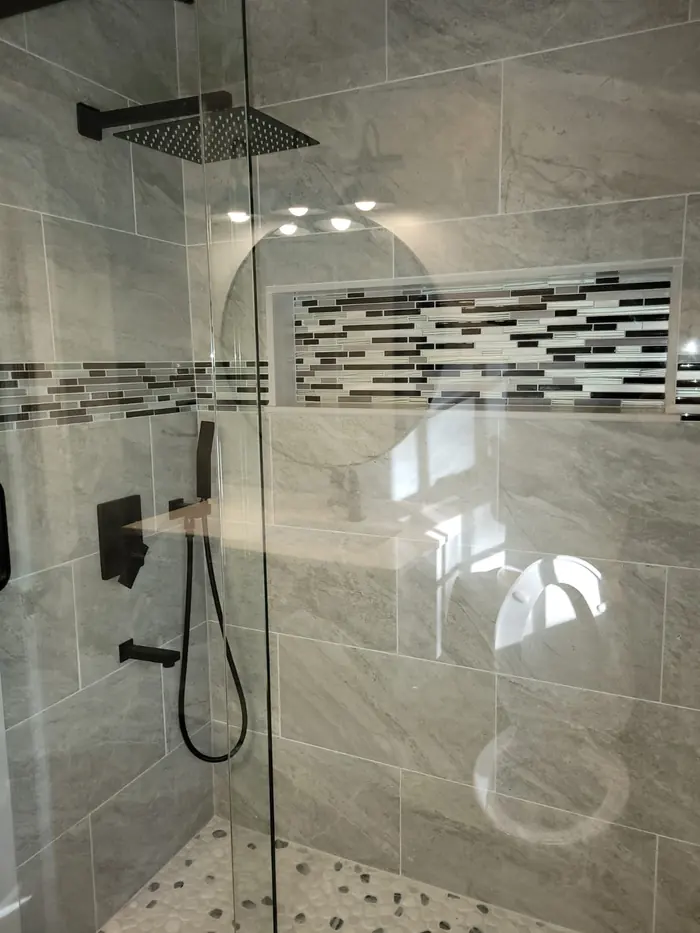 Walk-in shower with large grey porcelain tile, a glass and stone mosaic accent band, pebble floor and matte black rain shower head