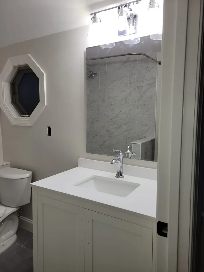 Bathroom with white vanity, chrome faucet and octagon window above the toilet